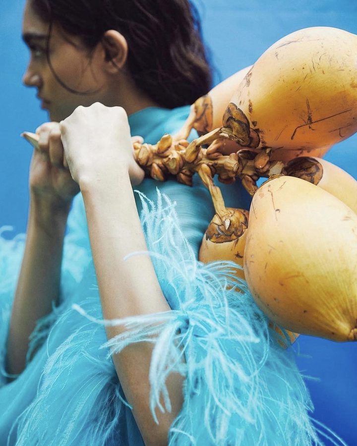 Model in turquoise feathers carrying king coconuts