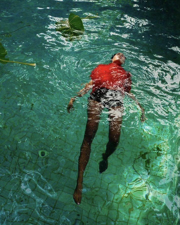 Model in red floating in a green-tiled pool