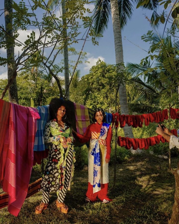 Two models among hanging textiles in a palm garden