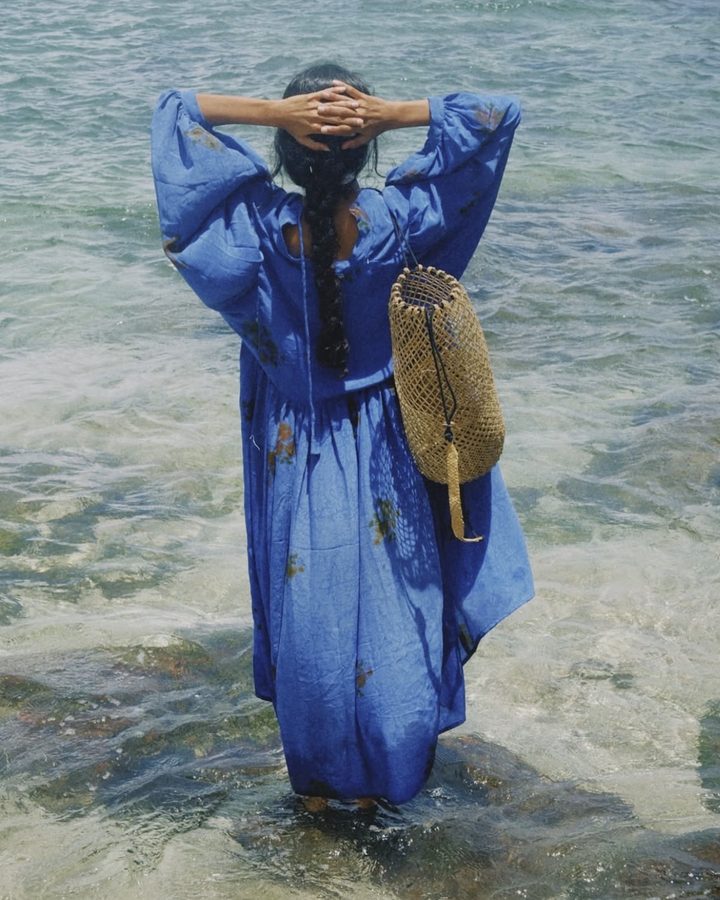 Model in a blue dress standing in the sea with a woven basket
