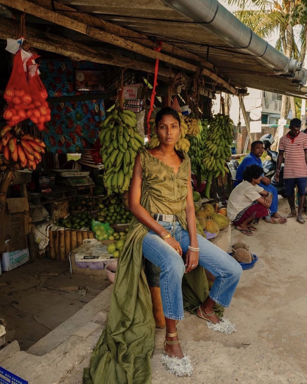 Model in an olive dress and denim at a fruit stall in Sri Lanka